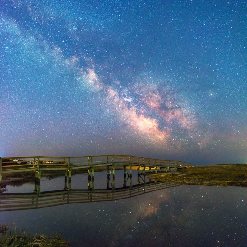 The Milky Way stretches over background with bridge in foreground.