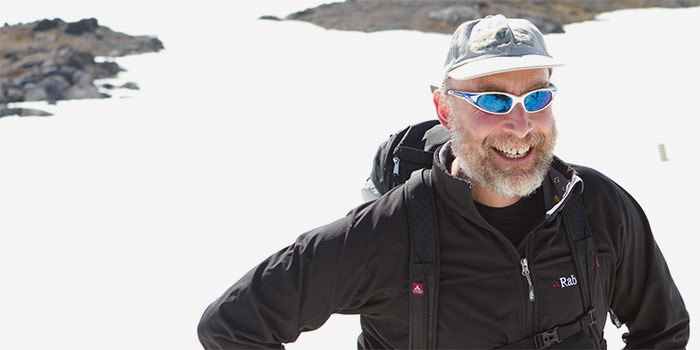 Bearded man in winter garbe and sunglasses smiling and standing on ice.