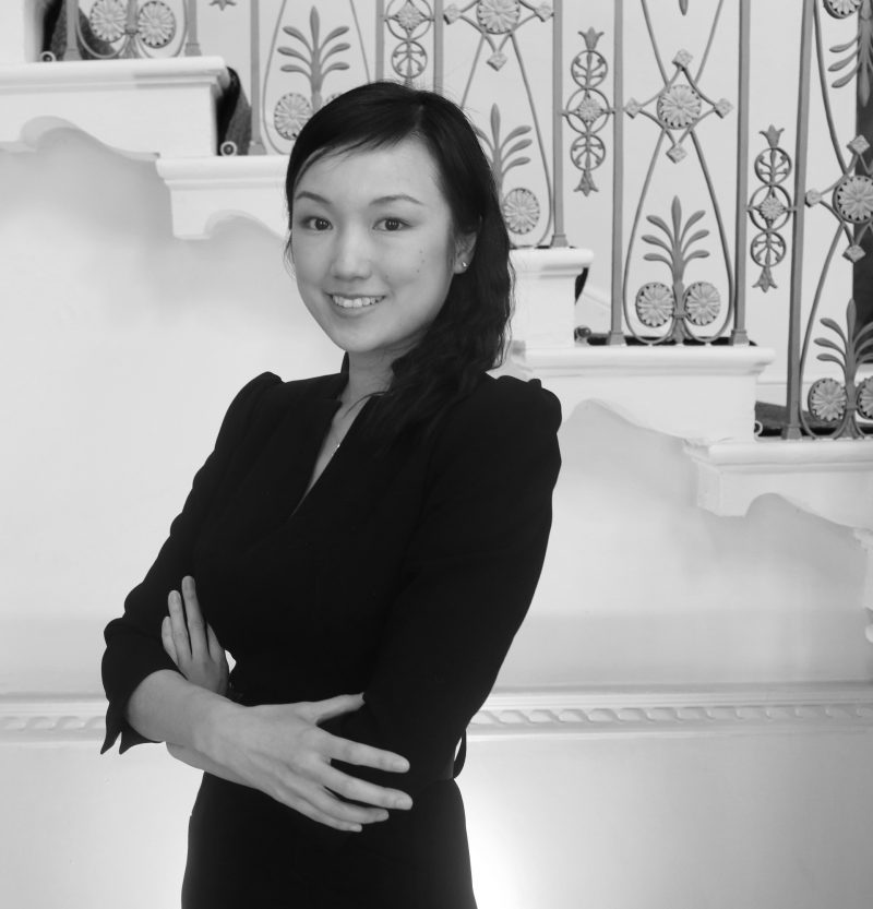 Smiling woman with arms folded in black and white photo.