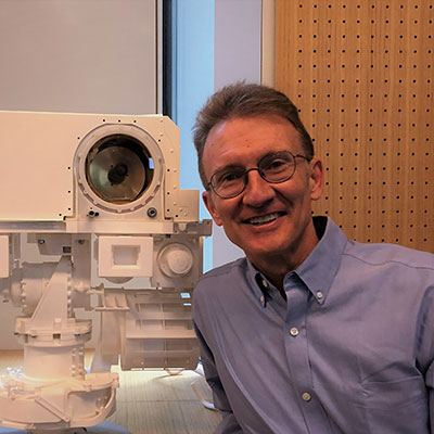 Smiling man standing next to tall robotic instrument with a big lense.