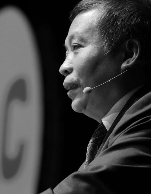 Profile of an Asian man speaking into a microphone.