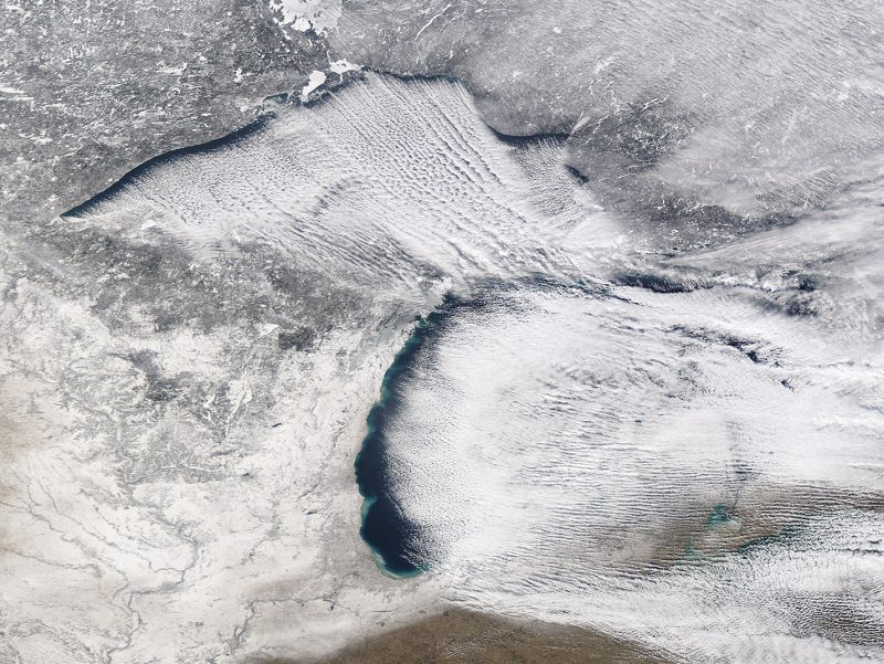 Orbital view of Great Lakes with clouds in thin parallel lines; entire region snow-covered.