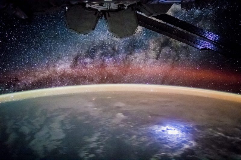 Starry night sky and curve of Earth's horizon from space with part of ISS visible.