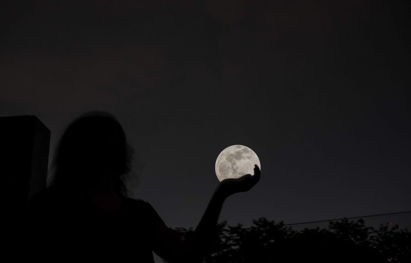 Silhouette of woman holding full moon in her hand.