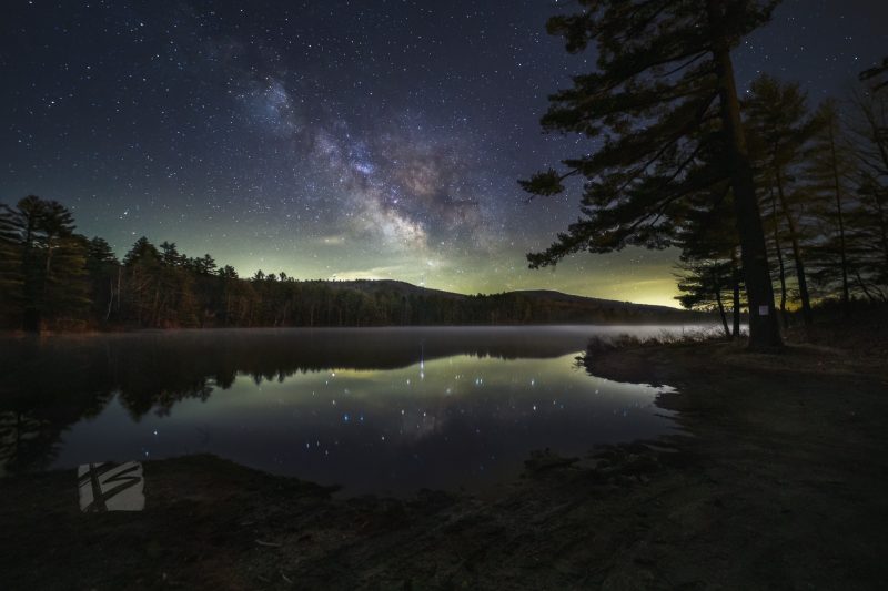 Starry cloud over lake with low-level fog, stars reflected in extremely calm lake.
