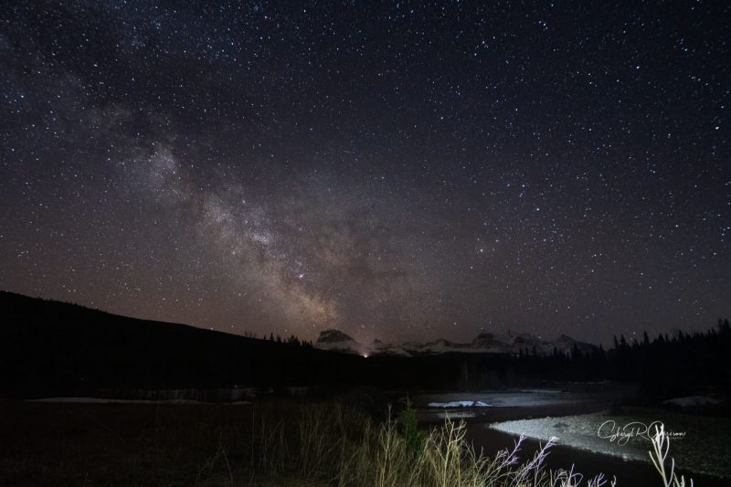 Milky Way cloud stretching across sky with rugged snow-capped mountains in the distance.