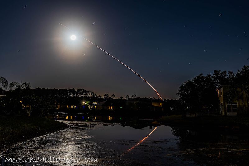 Bright light with aura, with a path of rocket seemingly heading towards it. Water in the foreground with the scene reflected.