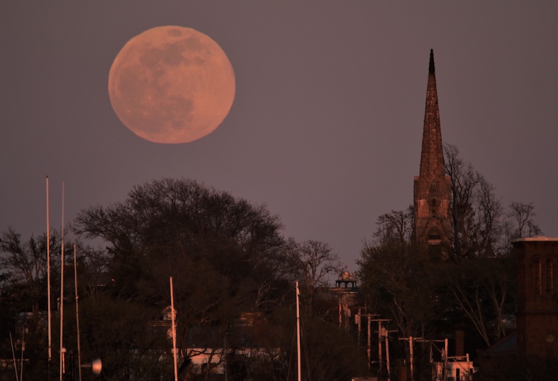 Pink large full moon next to an old church steeple.