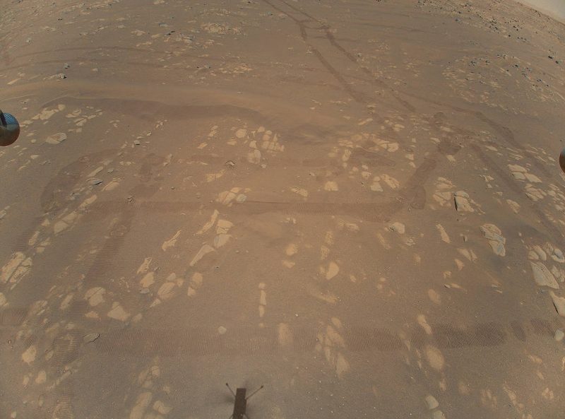 Square of patchy brown, with faint tracks visible and tiny shadow of helicopter.