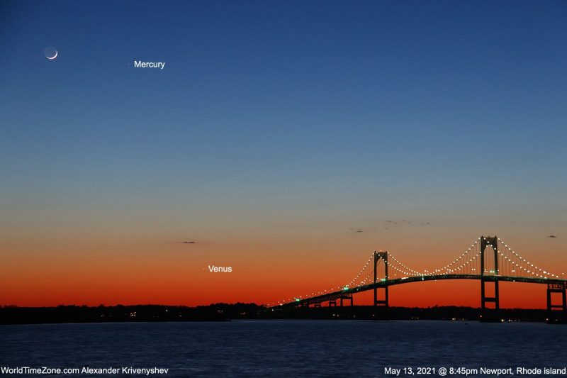 Crescent moon, 2 labeled dots (Mercury and Venus) in blue and orange sky over a lighted suspension bridge.