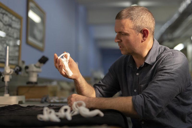 Man holding and examining a fossil bone in a lab.
