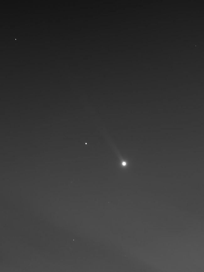 Dot of light with long, fuzzy, pale tail streaming to upper left.