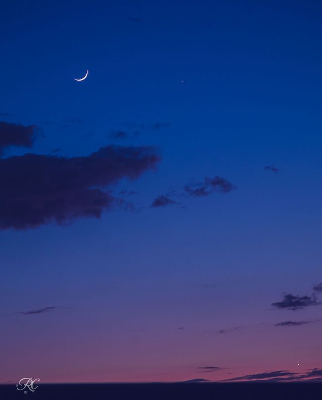 Purple to dark blue sky, with some clouds, a crescent moon at top left and bright dots of Mercury and Venus.