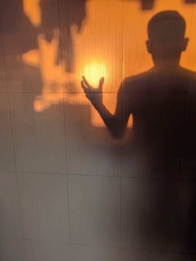 The shadow of a person appears as if holding the Singapore sun in light cast on a wall.