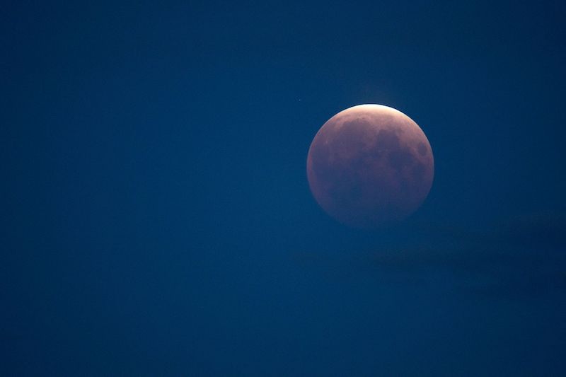 Lunar eclipse: shining orange and white moon on a dark blue sky background.