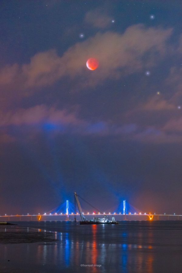 Orange moon above a lighted bridge.