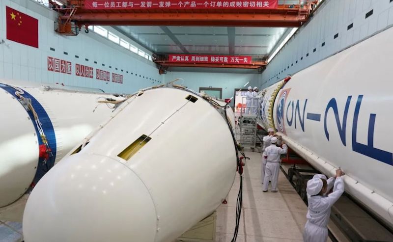 Staff in white uniforms are working in a room with giant, white rocket parts.