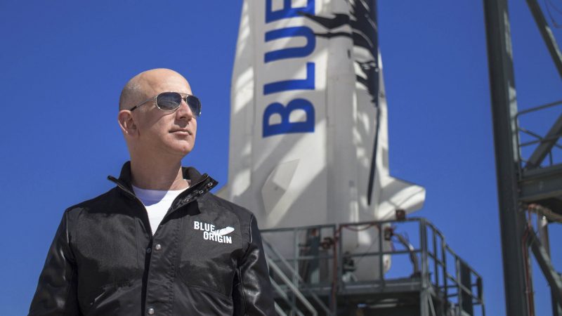 Launches: A bald man in sunglasses and a flight suit, standing in front of a rocket.