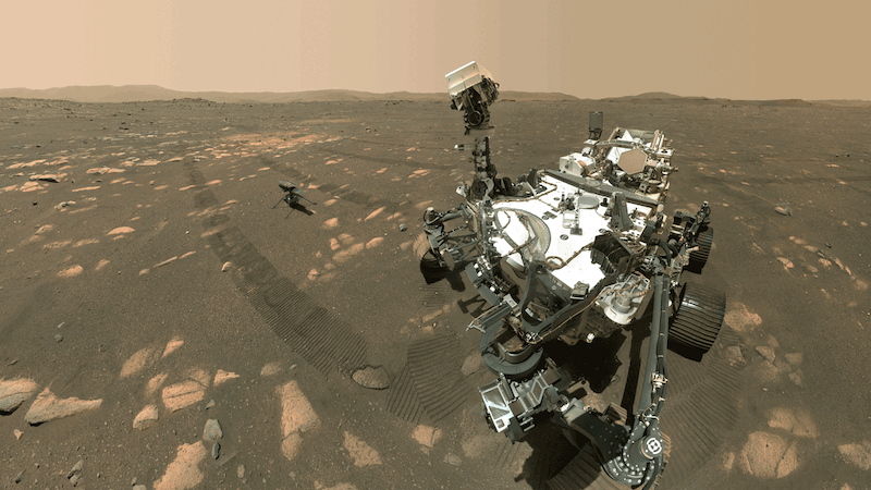 A large, white robot is pictured looking at the camera, then looking away at a smaller spacecraft in a brown, desert Mars landscape in this animated image.