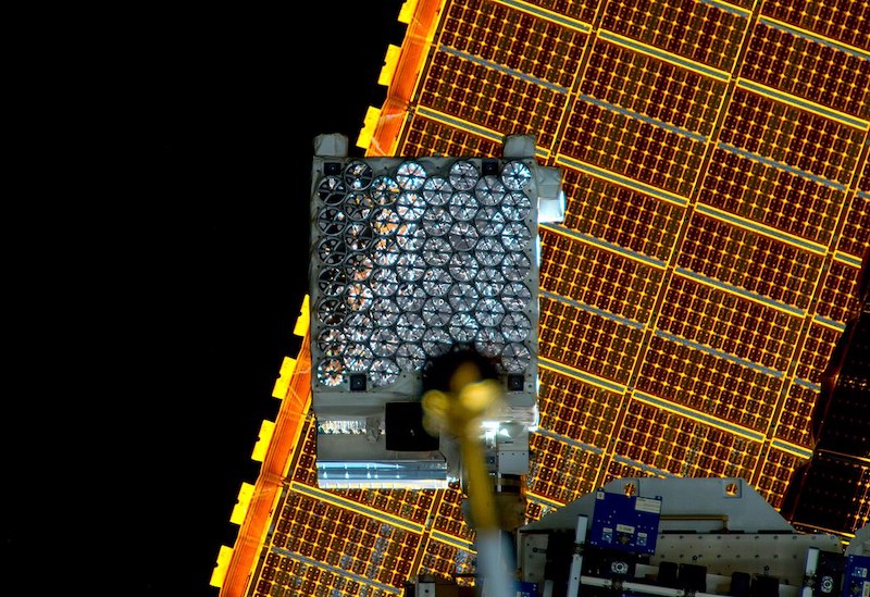 Telescope instrumentation mounted on the International Space Station, seen in front of solar panels. 