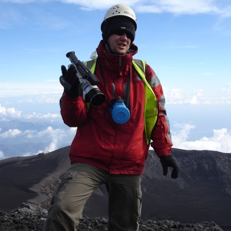 Man in hiking gear with clouds and barren mountain behind him.