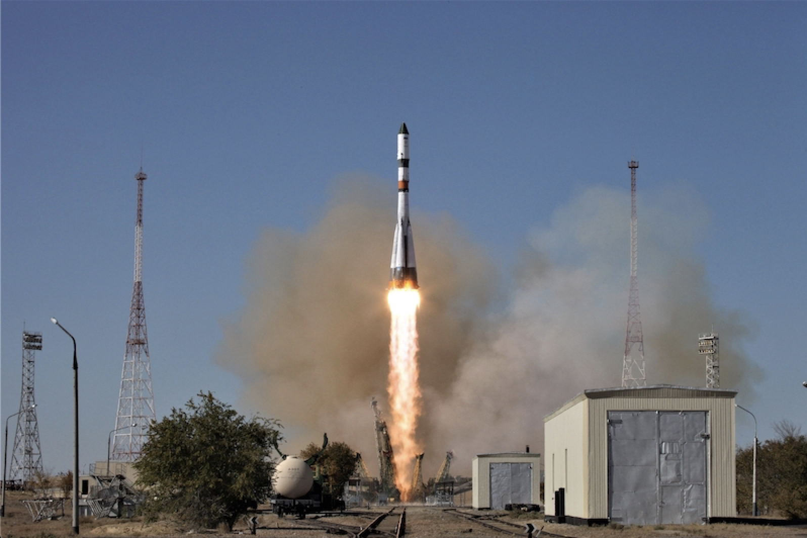 A white, skinny rocket shoots up into a pale blue sky from a desert landscape.