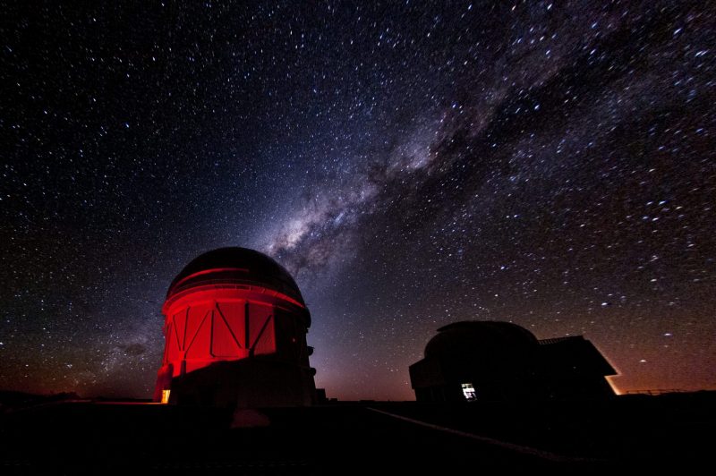 A red telescope dome under a dark sky, with the Milky Way arcing above.