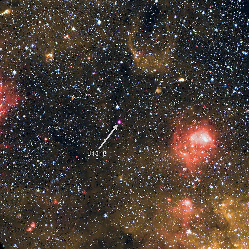 Dense star field with red and golden gas clouds and a central purple blob, a magnetar, pointed out by an arrow and annotated.