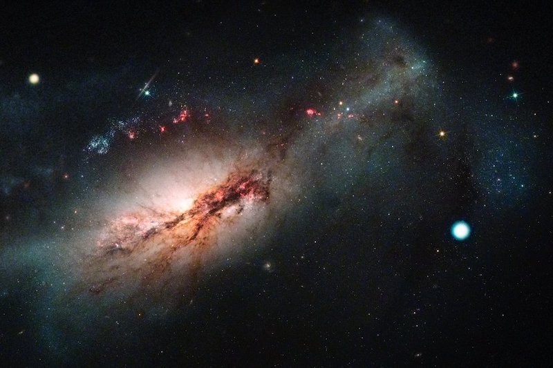Side view of olorful galaxy with dustbands, and the electron-capture supernova, a large bright dot nearby.