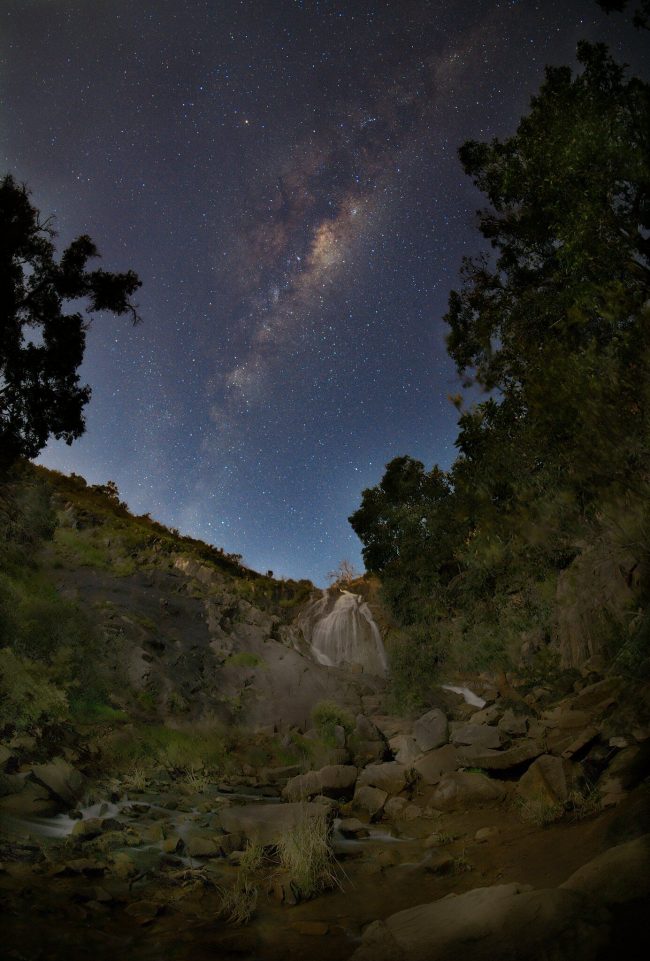 Arcing starry cloud over darkened waterfall.