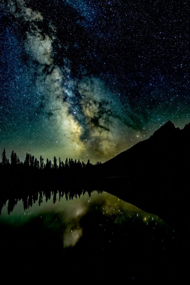 Dark clouds of Milky Way stretching up from lake and black mountain.