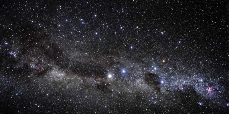 A wide view of a star field with a few bright stars and many faint ones and the Milky Way running across.