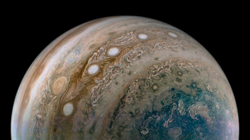 Planet Jupiter seen close up, with a string of 5 white ovals visible on its surface amid parallel swirly bands.