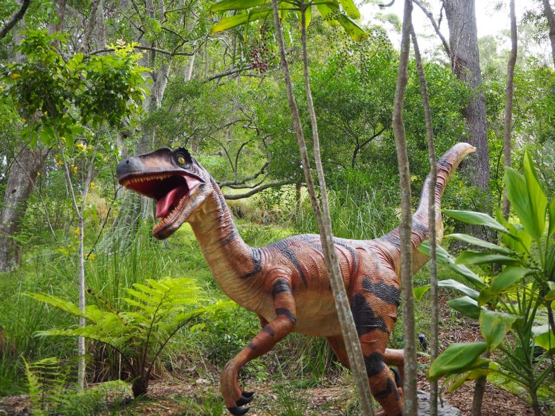 Recreate dinosaurs from their DNA: Striped predatory dinosaur with open mouth moving through trees.