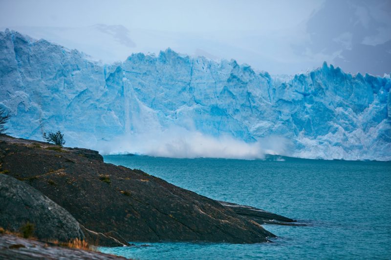 The 2021 IPCC report: Blue cliff of iceberg with splash into water.