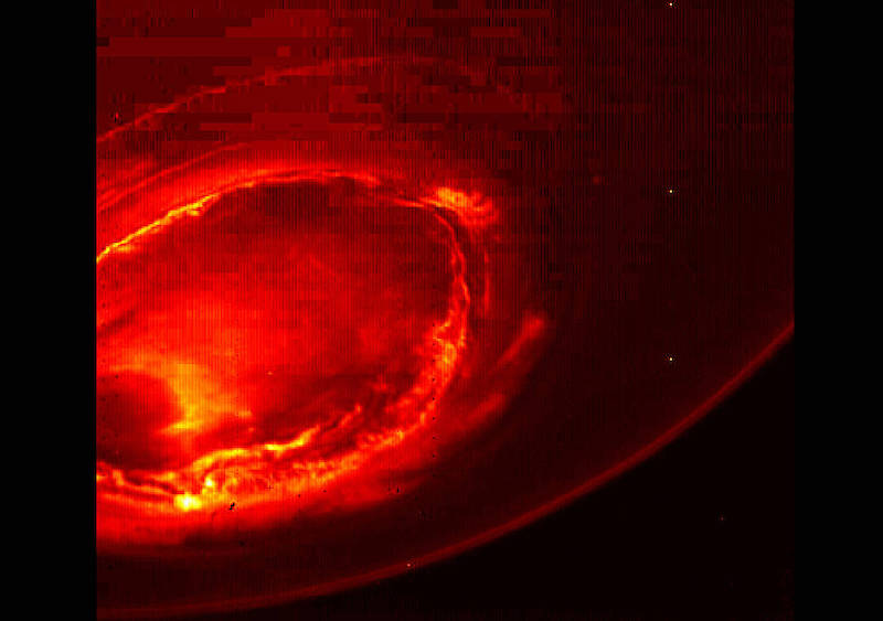Bright circular reddish ring on dark limb of planet.