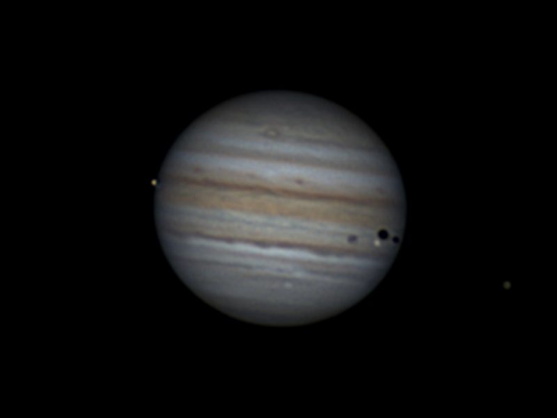 Jupiter with four moons and three shadows visible.