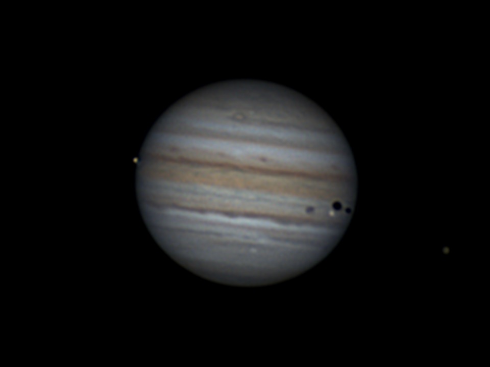 Jupiter with four moons and three black dot shadows visible.