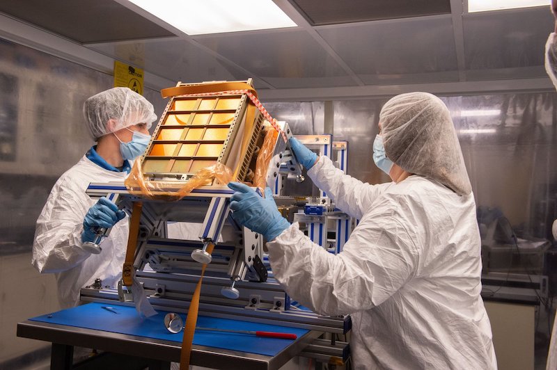 NEA Scout: Two people outfitted with white suits that cover their hair, hands, and bodies assemble a small golden spacecraft.