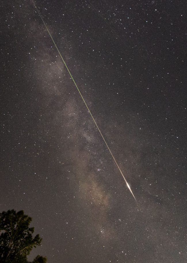 Starry Milky Way with long thin bright streak angling down through it with brilliant arrow-shaped lower end.