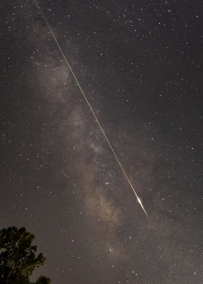 Cloudy starry Milky Way with meteor angling down through it, bright end.