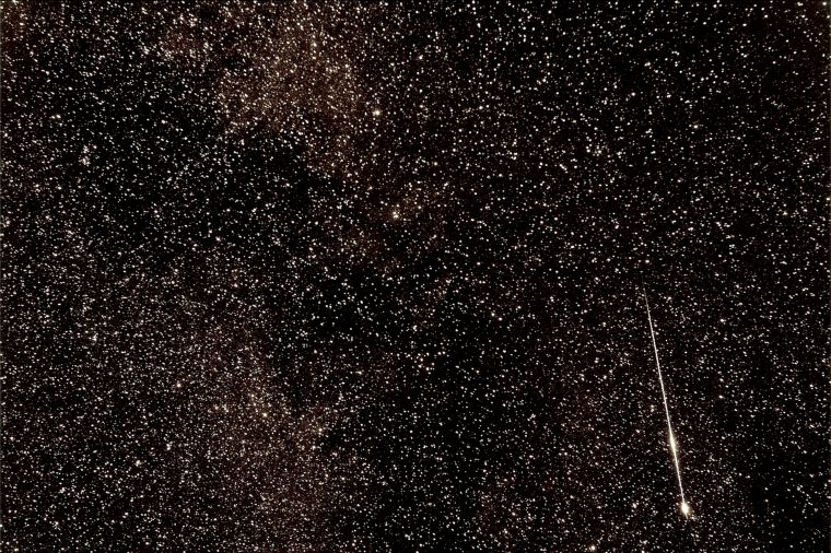 Close-up of very starry sky with bright meteor slash with two bright wider spots along the streak.