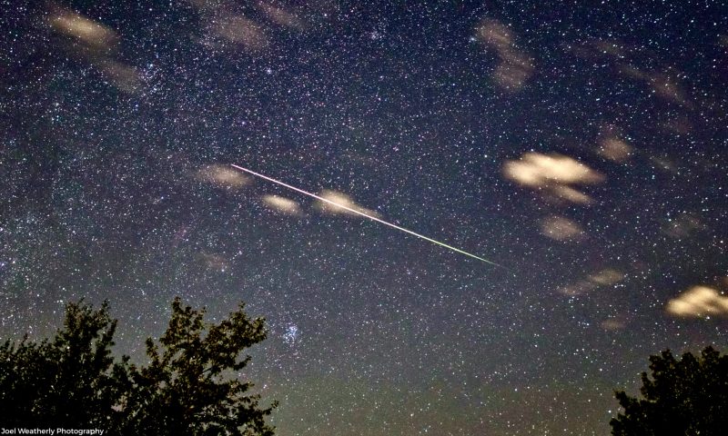 A few clouds and a thin, very bright meteor streaking across center of starry sky.