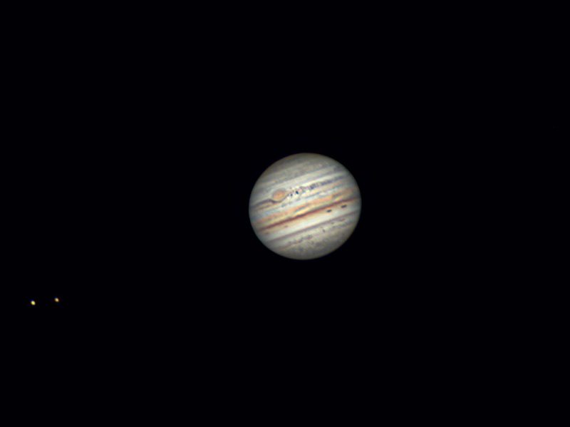 Jupiter with detailed bands and red spot, with 2 little dots of light (its moons) nearby.