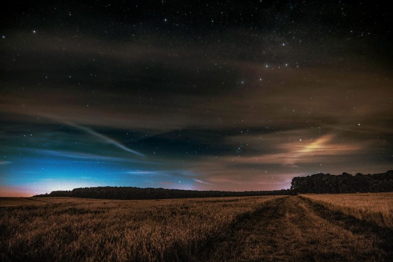 Broad agricultural fields, with Cassiopeia shining through wispy clouds.
