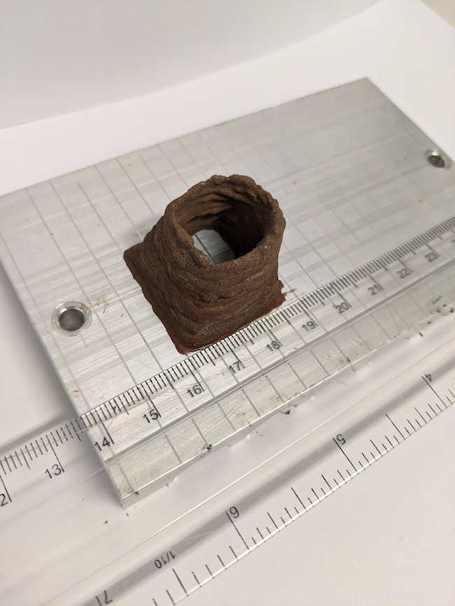 Small brown hollow 'chimney' of space concrete, built up on a metal surface, with a ruler next to it.