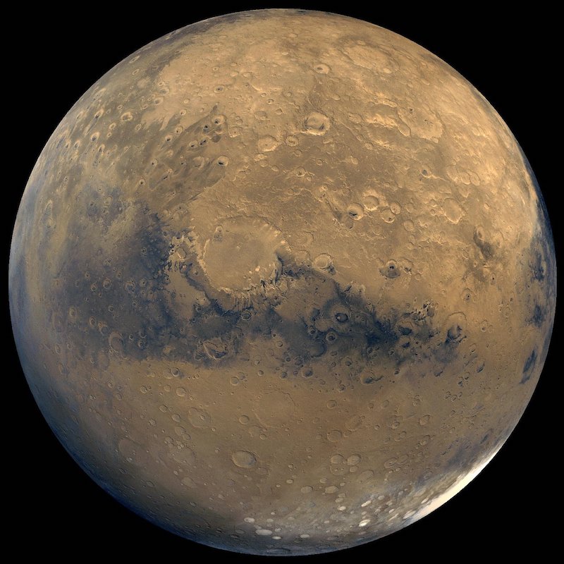 Reddish rocky planet with dark patches and bright white polar cap in lower right.