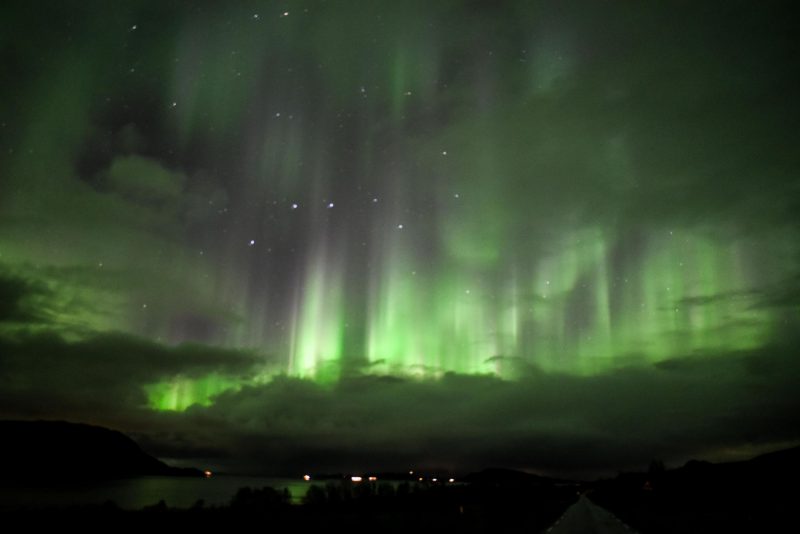 Big Dipper stars shine through the glow of green vertical aurora.