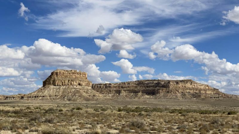 Blue sky with white clouds over dry landscape including a rocky butte.
