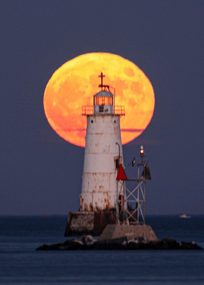 Big full moon behind a lighthouse.